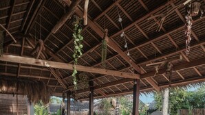 An outdoor lounge area with wooden furniture, cushions, and hanging plants. - Happiness Beach Resort Siargao (General Luna)