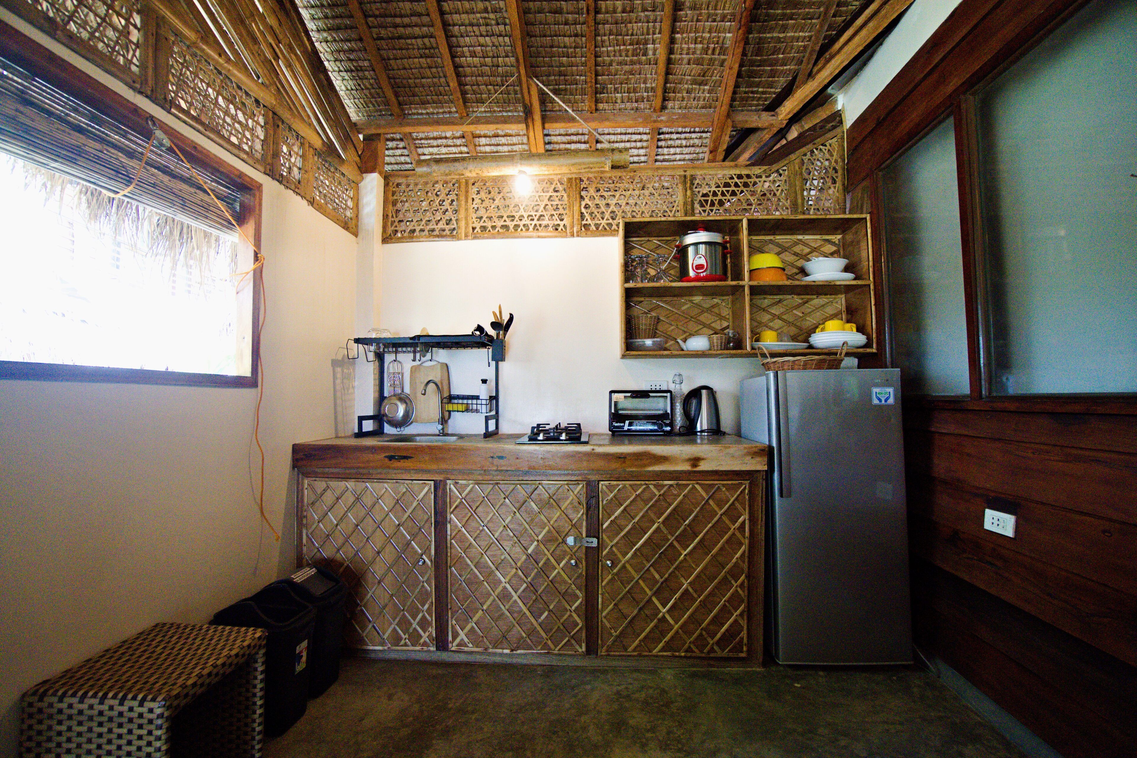 A compact kitchen with a refrigerator, a radio, and a shelf with dishes.