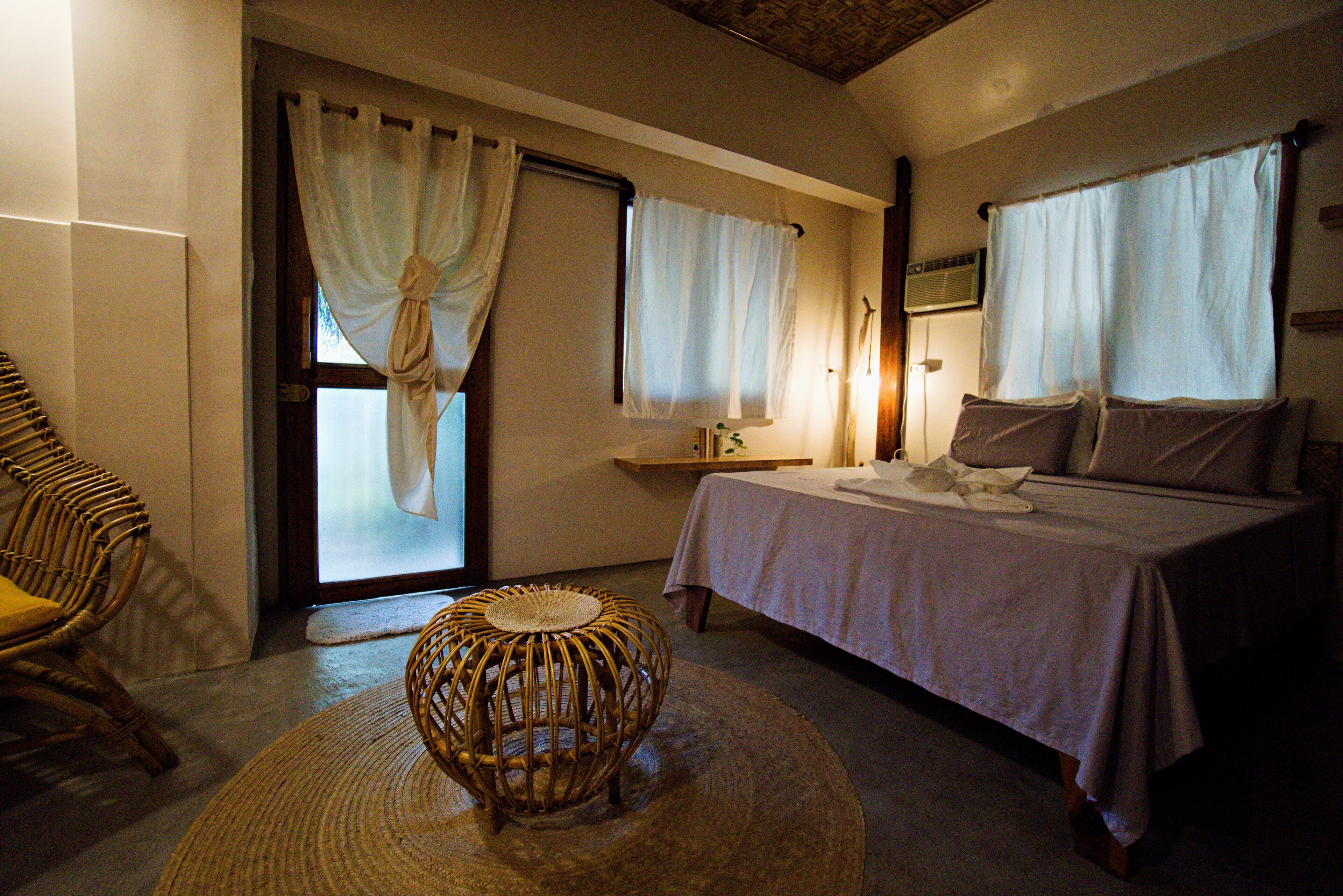A bedroom with a bed, a wicker chair, and a small round table.