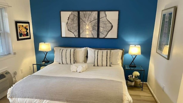 A bedroom with a large bed, two bedside tables with lamps, a blue accent wall, and artwork above the bed.