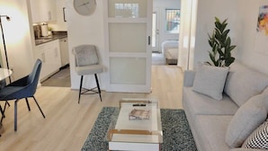 A modern living room with a sofa, a coffee table, a chair, and a kitchen area visible through an open door.