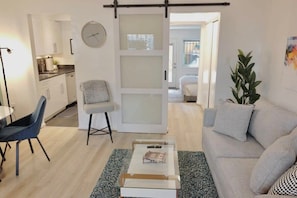 A modern living room with a sofa, a coffee table, a chair, and a kitchen area visible through an open door.