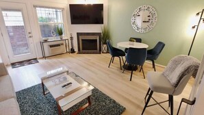 A modern living room with a glass coffee table, a fireplace, a TV, and a dining area with chairs.