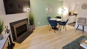 A living room with a fireplace, a dining area with a round table and chairs, and a kitchen in the background.