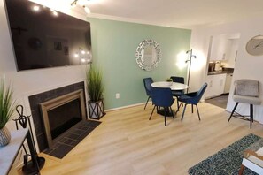 A living room with a fireplace, a dining area with a round table and chairs, and a kitchen in the background.