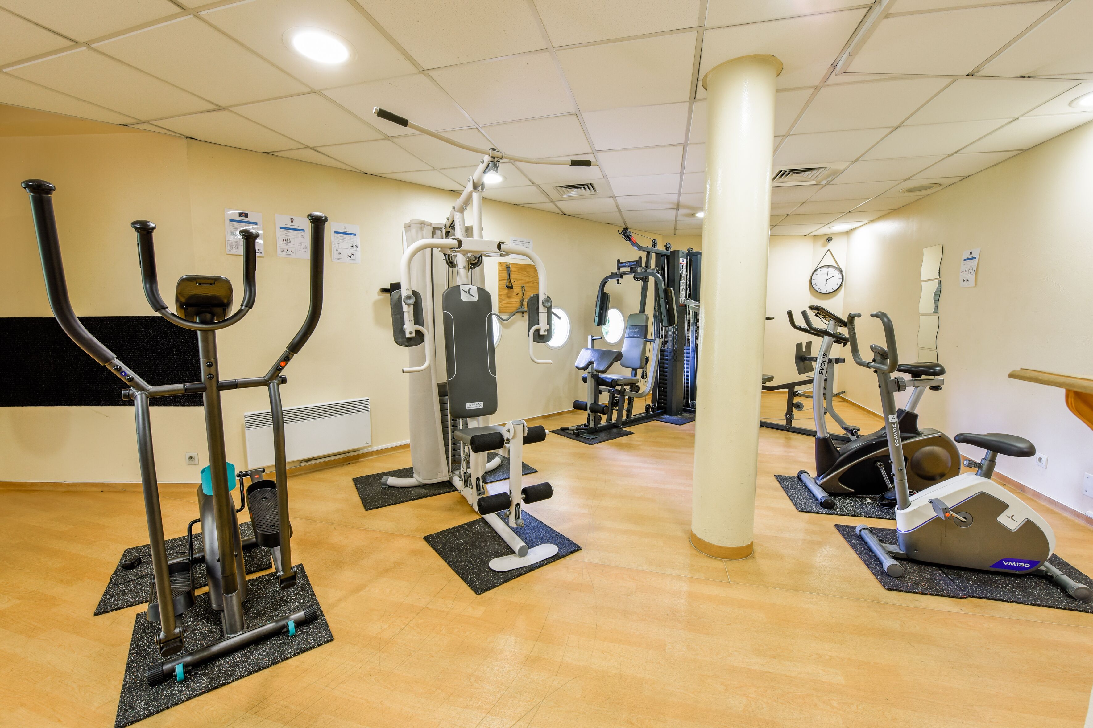 A gym with various exercise machines, mats, and a clock on the wall.
