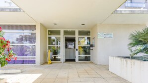 A building entrance with a tiled floor, glass doors, and a sign indicating directions. - Résidence Columba  (Agen)