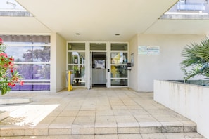 A building entrance with a tiled floor, glass doors, and a sign indicating directions. - Résidence Columba  (Agen)