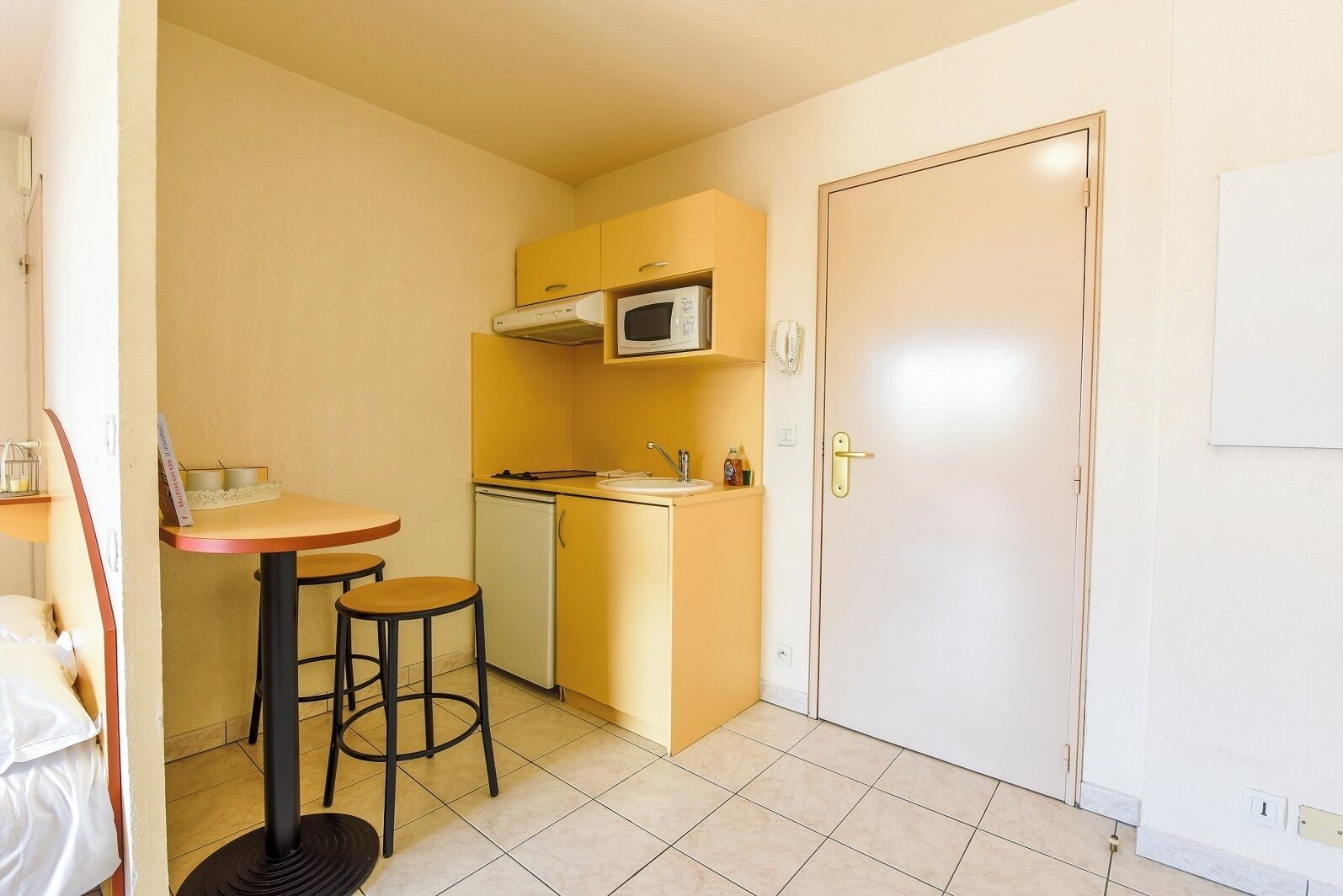 A compact kitchen with a microwave, sink, and a small dining area with stools.
