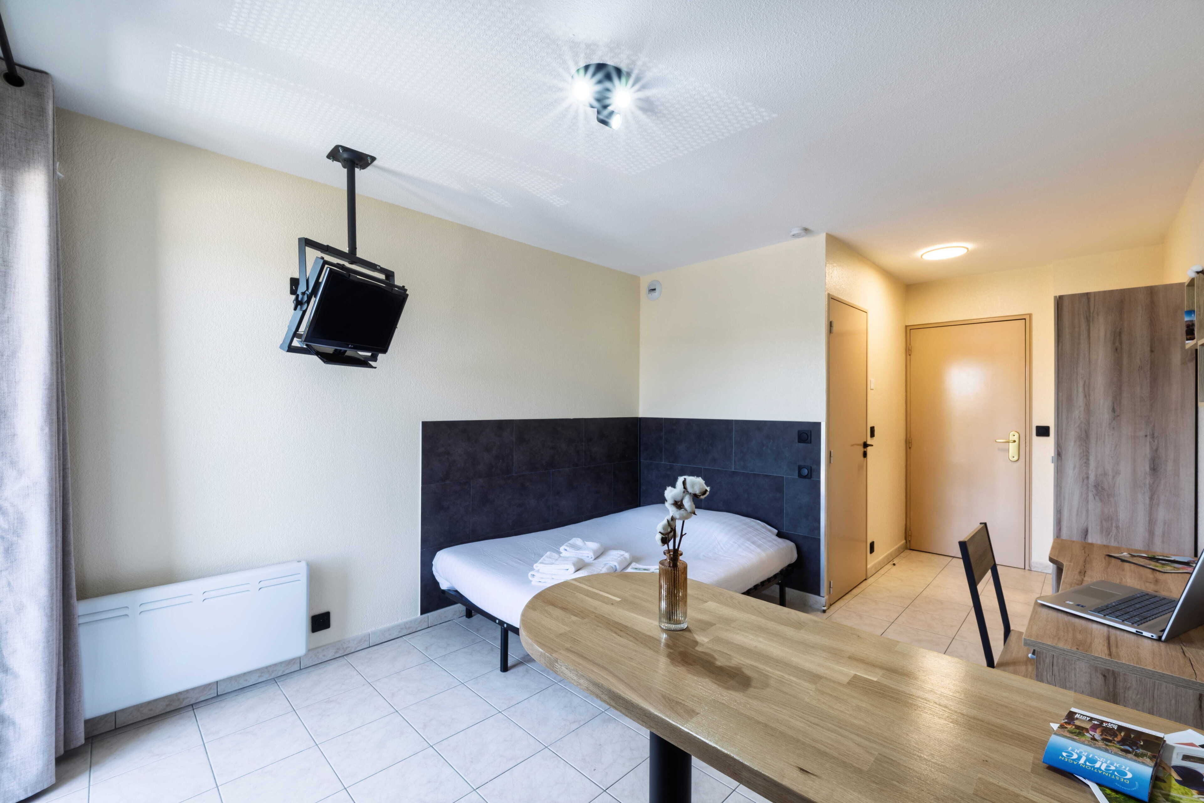 Una camera d'albergo con un letto, una scrivania, un portatile, una televisione montata a parete e una porta.