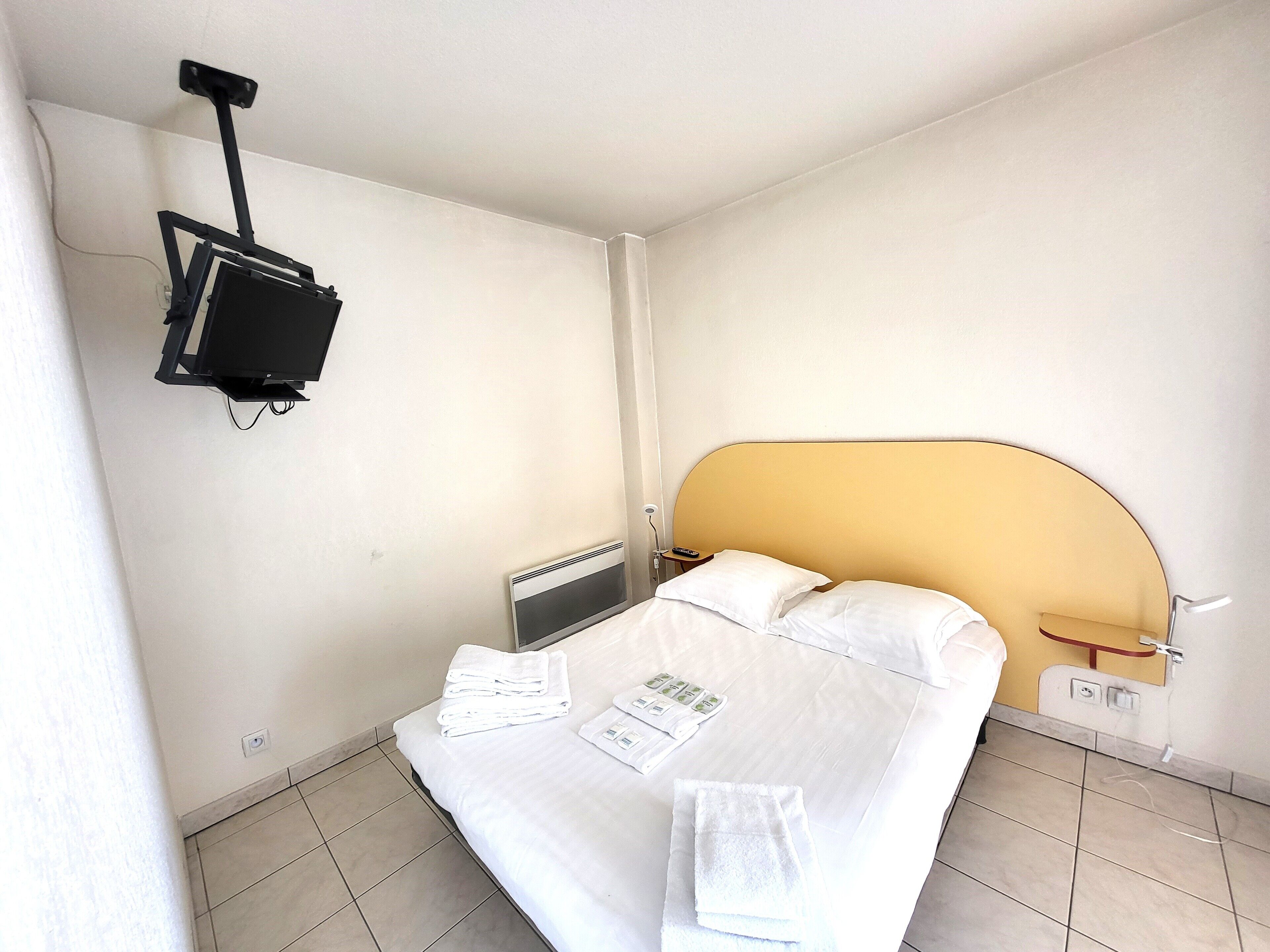 A hotel room with a bed, a bedside table, a wall-mounted TV, and a radiator.