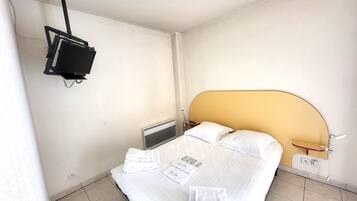 A hotel room with a bed, a bedside table, a wall-mounted TV, and a radiator.