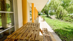 A covered outdoor seating area with wooden benches and yellow pillars, overlooking a grassy area with trees. - Résidence Columba  (Agen)