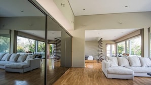 A modern interior with a large mirror reflecting a room, a wooden floor, and a white sofa. - Studio Rio Unique Space With Garden and Garage (Patras)