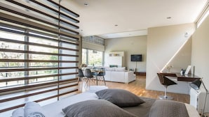 A modern living room with a sofa, a dining area, and a TV mounted on the wall. - Studio Rio Unique Space With Garden and Garage (Patras)