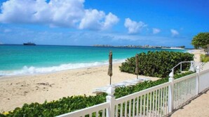 A beach view with a white fence, umbrellas, and a ship in the distance. - Beachfront condo with pool (Simpson Bay)