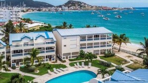 A resort with multiple buildings, a swimming pool, and a beach with boats. - Beachfront condo with pool (Simpson Bay)