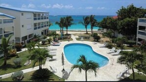 A resort with a swimming pool, palm trees, and a view of the ocean. - Beachfront condo with pool (Simpson Bay)