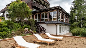 A house with a balcony, a wooden deck, and a sandy area with lounge chairs. - stuub hinterzarten (Breitnau)