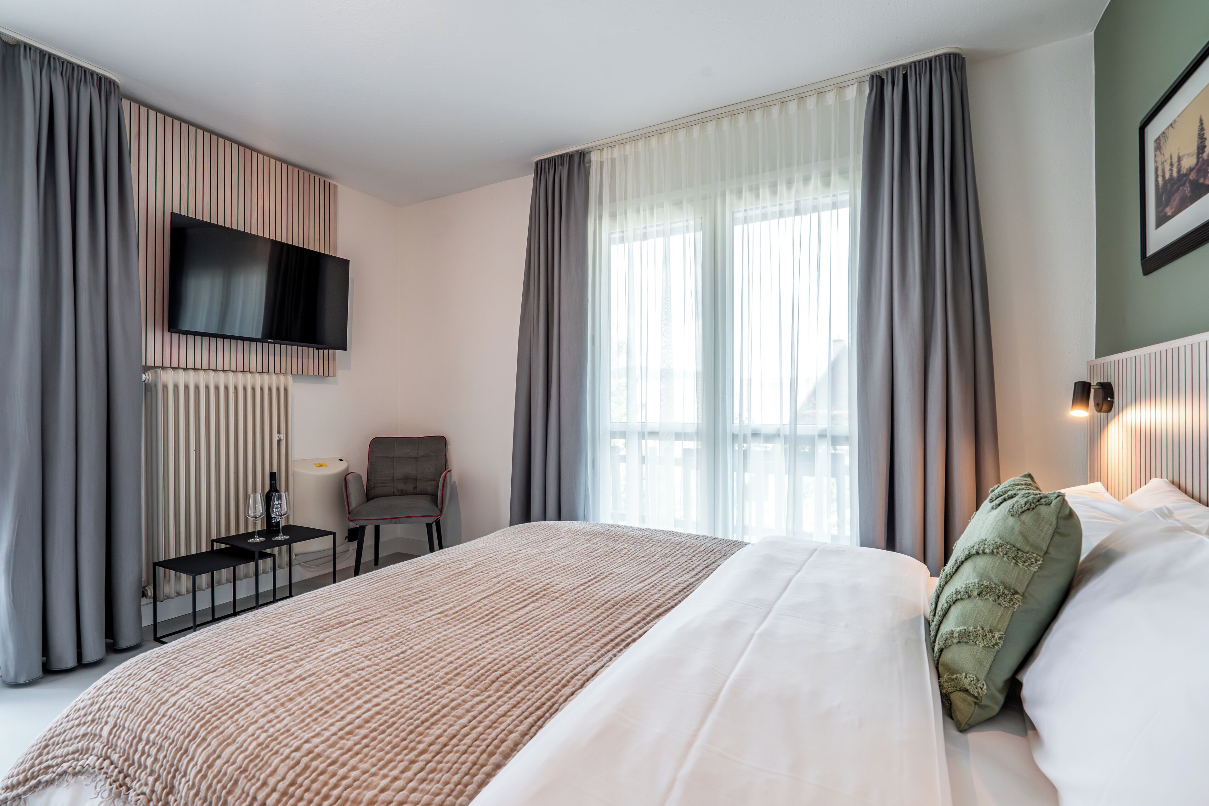 Une chambre d’hôtel avec un grand lit, un téléviseur à écran plat fixé au mur, une petite table avec une lampe et une chaise.