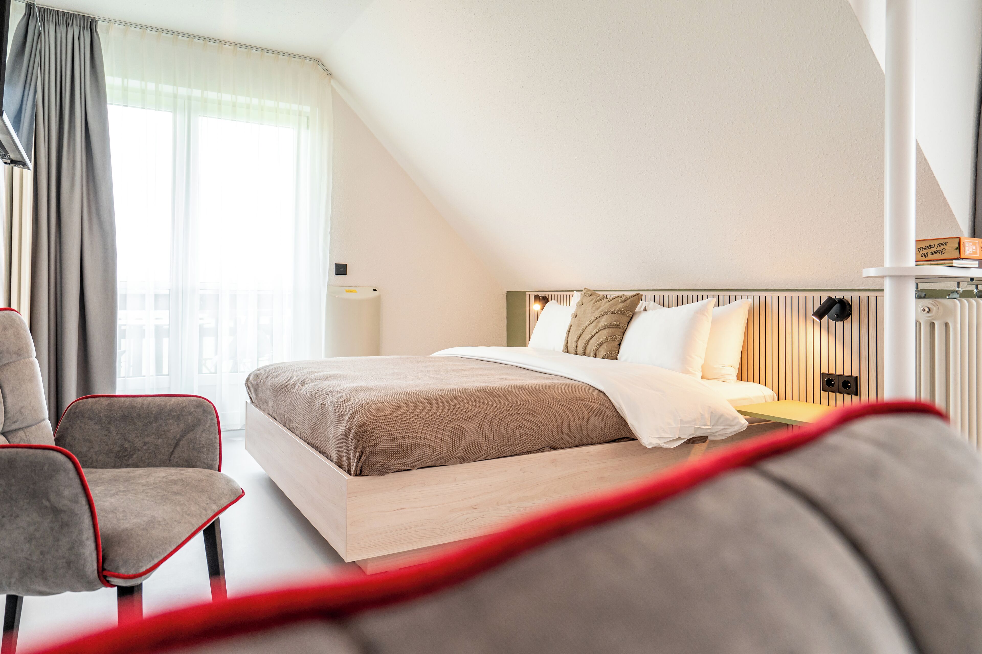 A modern hotel room with a bed, a chair, and a view of the outdoors.