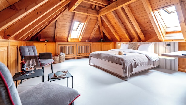 A high-ceilinged attic bedroom with a large bed, two chairs, a small table, and a window. - stuub hinterzarten (Breitnau)
