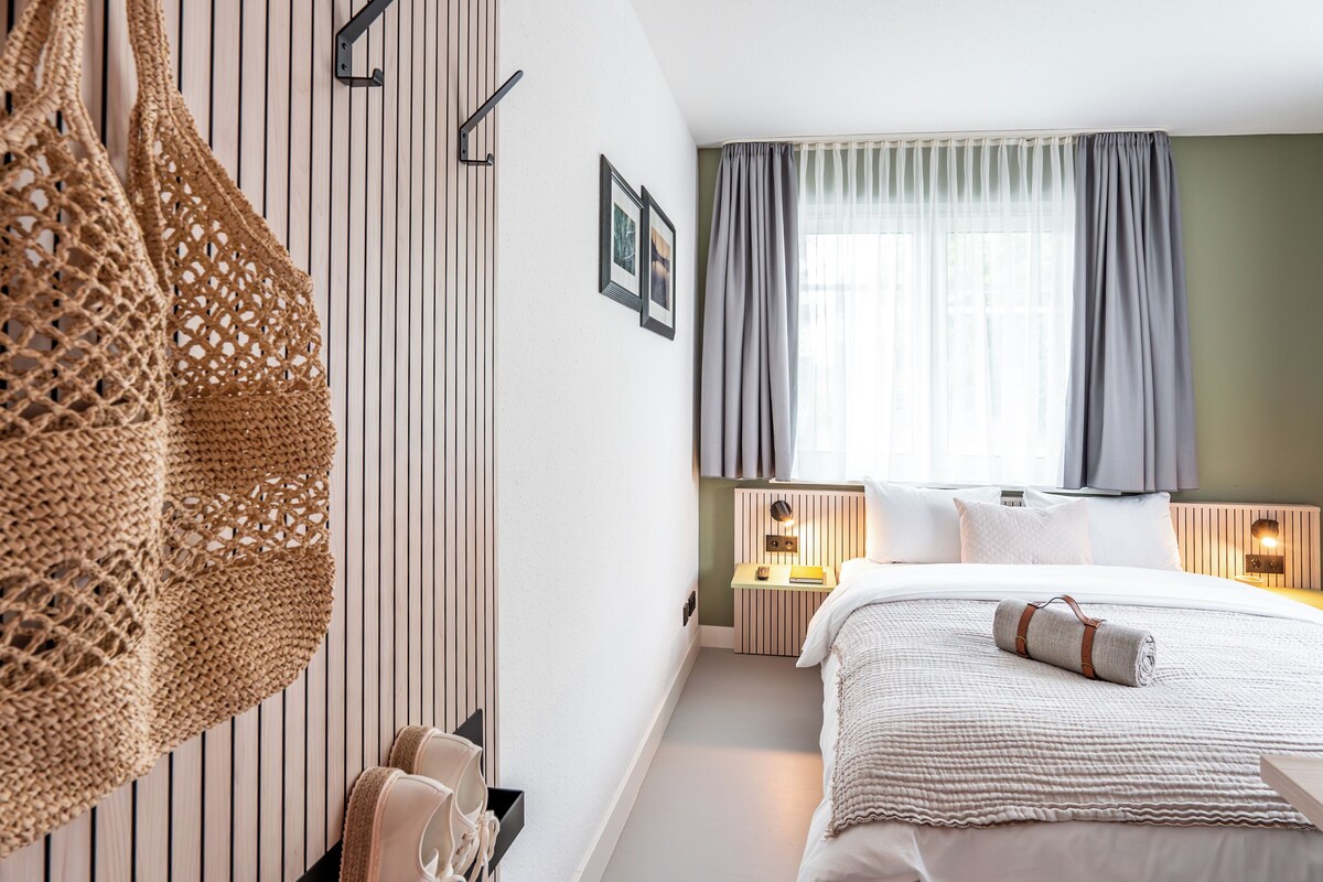 A hotel room with a bed, bedside tables, a wall-mounted rack, and a window with curtains.