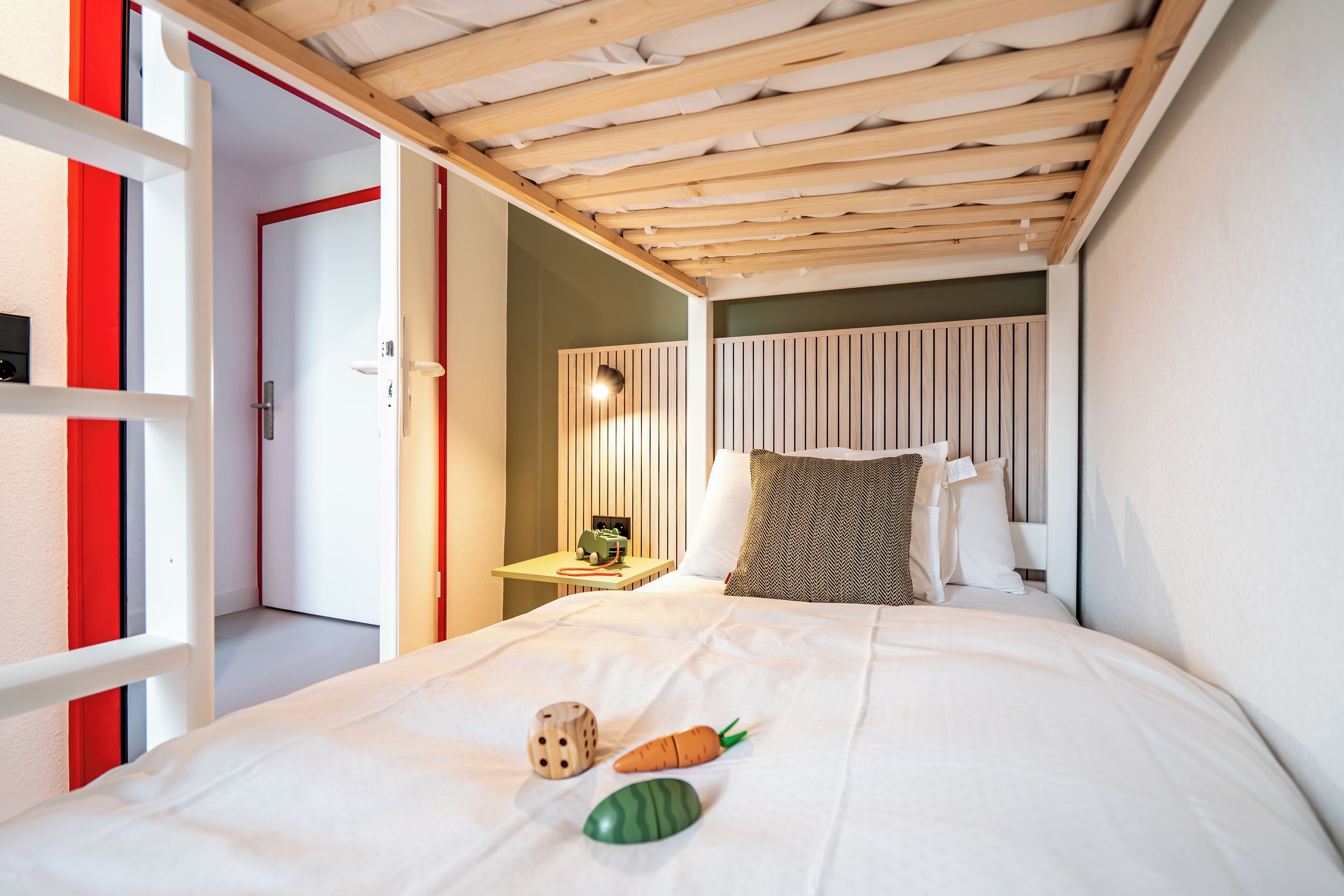 A bedroom with a wooden ceiling, a bed with white bedding, a nightstand with a lamp, and a door with red trim.