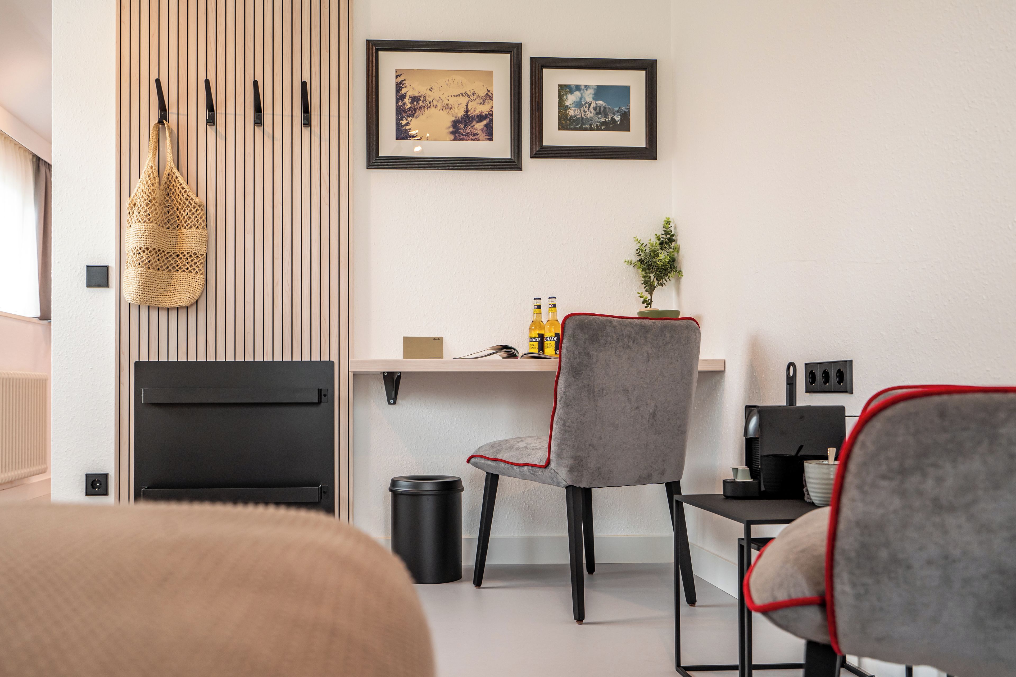 A modern living room with a sofa, a dining area with a table and chairs, and a wall-mounted shelf with books and bottles.