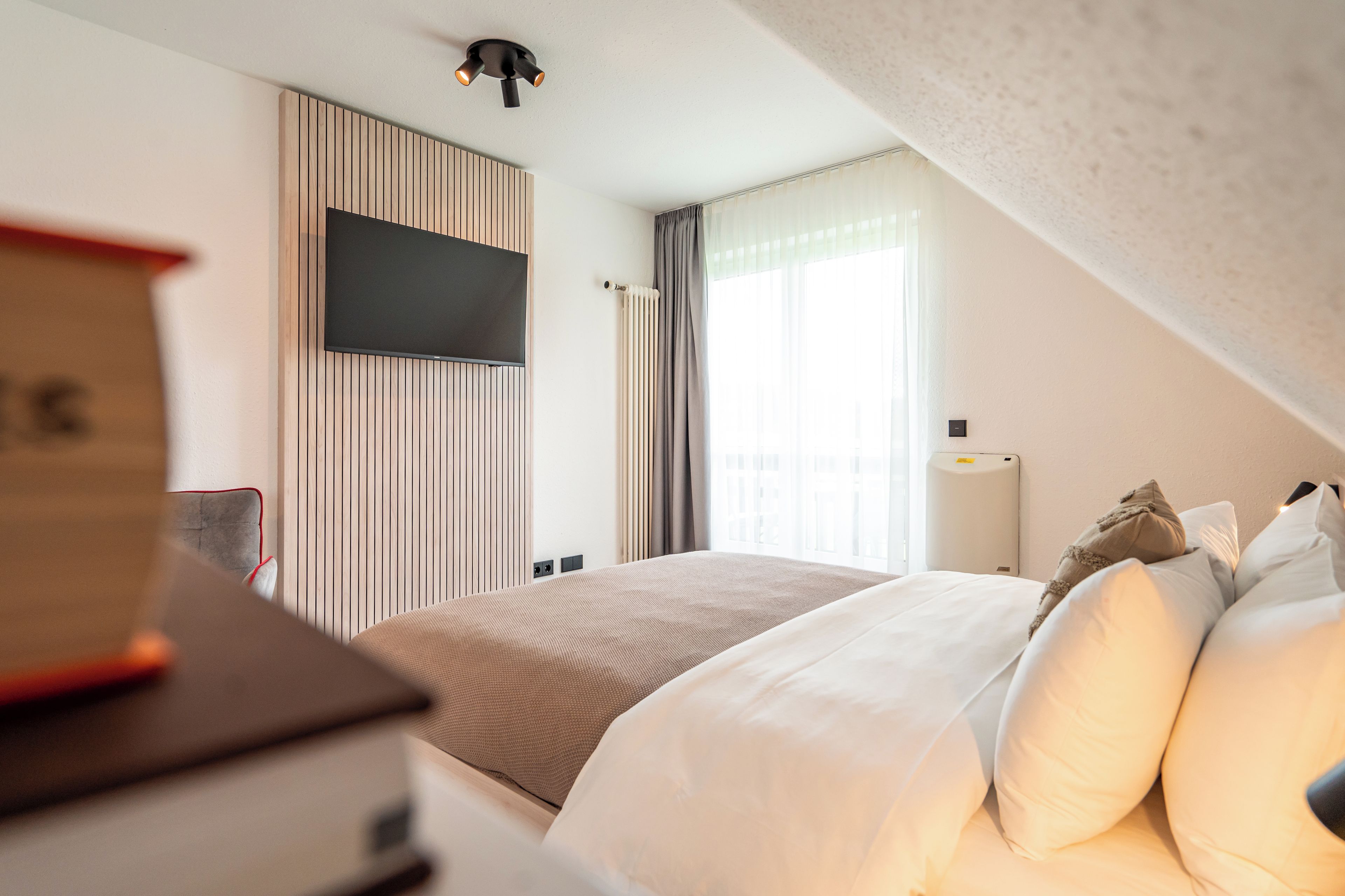 Habitación de hotel con cama, televisor montado en la pared y ventana con cortinas.