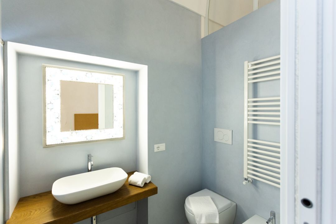 A bathroom with a wooden vanity, a white sink, a mirror with a light, a towel, a toilet, and a white towel rack.