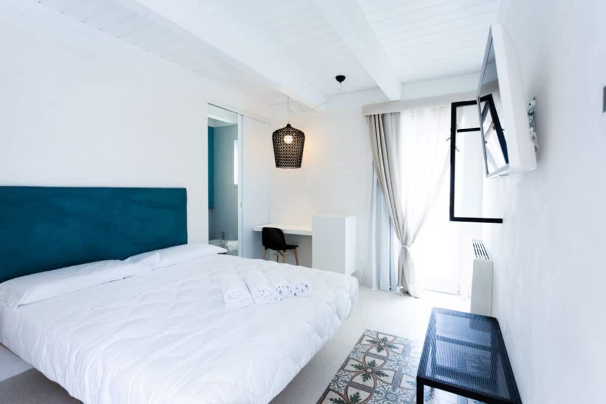 A modern bedroom with a large bed, a desk, and a TV mounted on the wall.