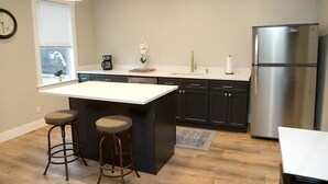Una cocina moderna con una isla central, armarios oscuros, electrodomésticos de acero inoxidable y dos taburetes de bar.