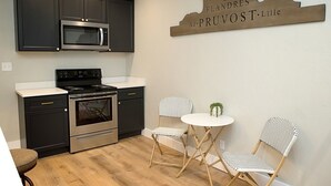 Una cocina moderna con armarios oscuros, un microondas de acero inoxidable, una estufa y un pequeño comedor con dos sillas y una mesa.