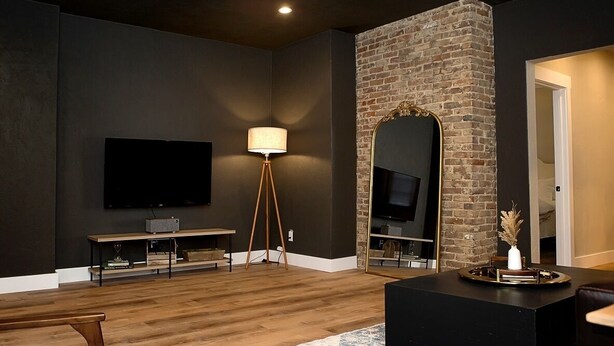 Una sala de estar moderna con un televisor de pantalla plana, una lámpara de pie, un espejo grande y una pared de ladrillo decorativa.