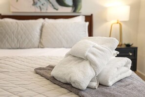 A neatly made bed with a quilted cover, a stack of folded white towels, and a bedside lamp on a nightstand.