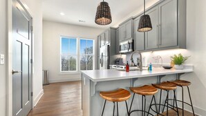 Une cuisine moderne avec des meubles gris, un îlot central blanc doté de tabourets et un éclairage suspendu.