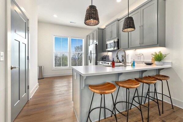 A modern kitchen with grey cabinets, a white island with stools, and pendant lighting.
