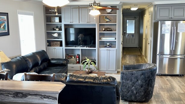 A modern living room with a leather sofa, a coffee table, and a TV. There is a kitchen area with a refrigerator and cabinets. - The Pearl - Beautiful, renovated Houseboat in Venice Marina!  (Venice)