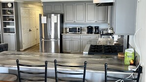 A modern kitchen with grey cabinets, stainless steel appliances, a marble countertop, and a bar area with chairs. - The Pearl - Beautiful, renovated Houseboat in Venice Marina!  (Venice)