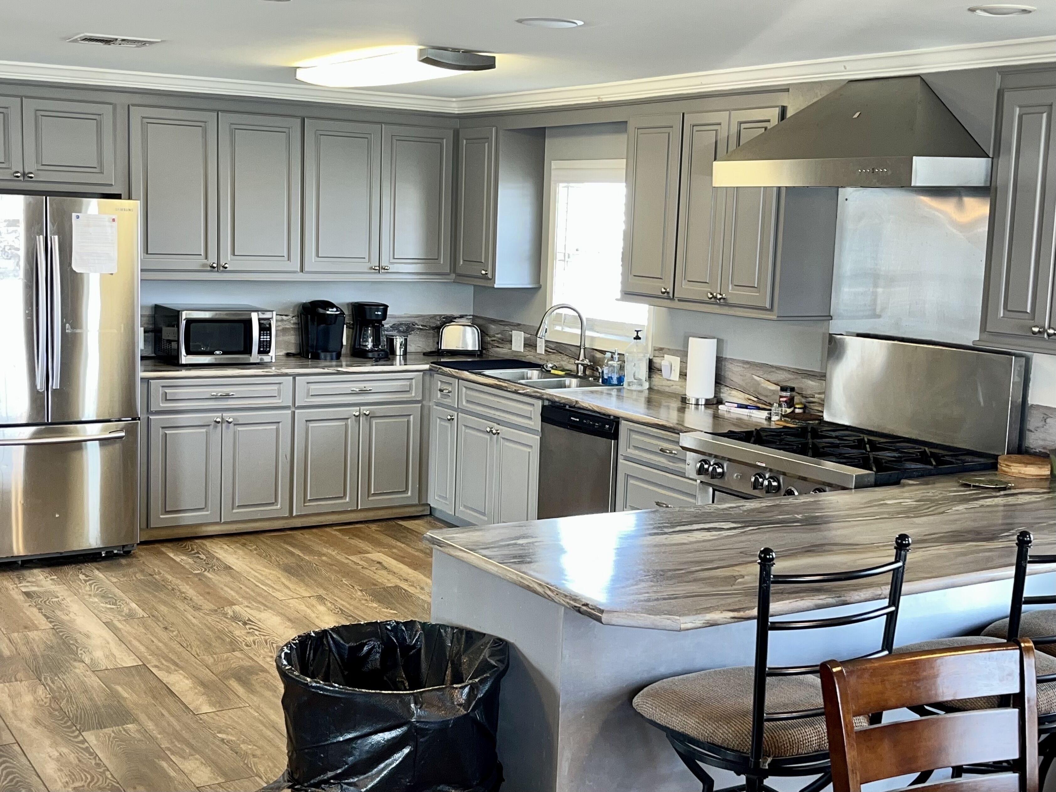 A modern kitchen with grey cabinets, stainless steel appliances, and a marble countertop.