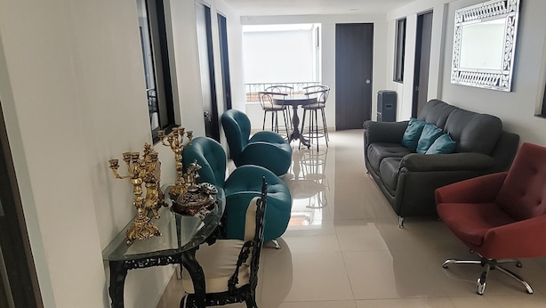 Un salón moderno con un sofá negro, un sillón rojo y una mesa de centro de cristal con candelabros de latón ornamentado.
