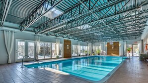 Uma piscina interior com teto alto, amplas janelas e chão revestido de azulejos.