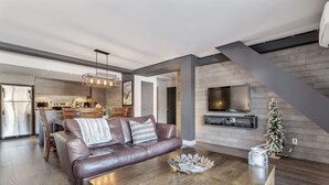 Uma sala de estar moderna com um sofá de couro, uma mesa de centro de madeira e uma TV fixada na parede.