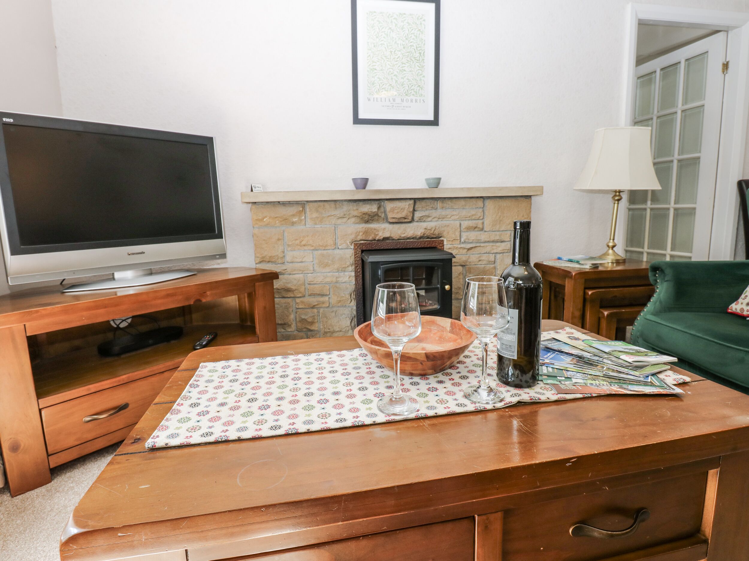 Sala de estar com televisão, lareira, móveis de madeira e uma mesa com copos de vinho e garrafa.