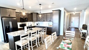 Una cocina moderna con una isla central, sillas blancas y una mesa de comedor con un posavasos.