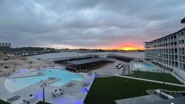 Un hotel con una amplia piscina al aire libre, una zona cubierta y vistas al atardecer sobre el agua.