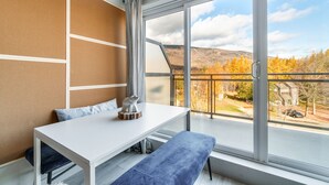 Ein modernes Zimmer mit einem weißen Tisch, einer blauen Bank und Blick auf buntes Herbstlaub durch große Fenster.