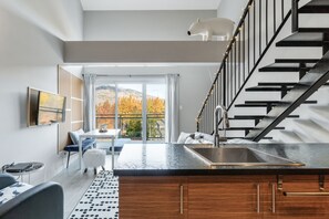Cocina moderna con encimera negra, pileta de acero inoxidable y escalera decorada con un oso blanco.