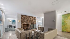 Ein modernes Wohnzimmer mit Kamin aus Stein, beigen Sofas und einem großen abstrakten Gemälde an der Wand.